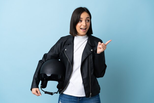 Donna che tiene un casco del motociclo isolato su priorità bassa blu che intende realizzare la soluzione mentre solleva un dito