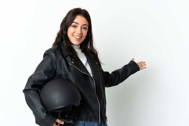 Donna che tiene un casco del motociclo su bianco che estende le mani a lato per invitare a venire