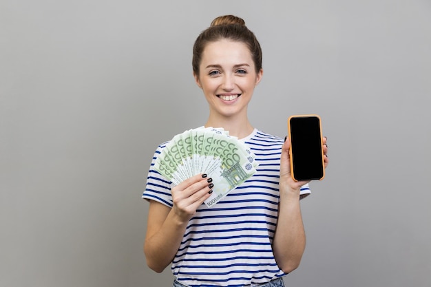 Donna che tiene un fan di banconote in euro e smartphone con schermo vuoto nero che fa soldi online