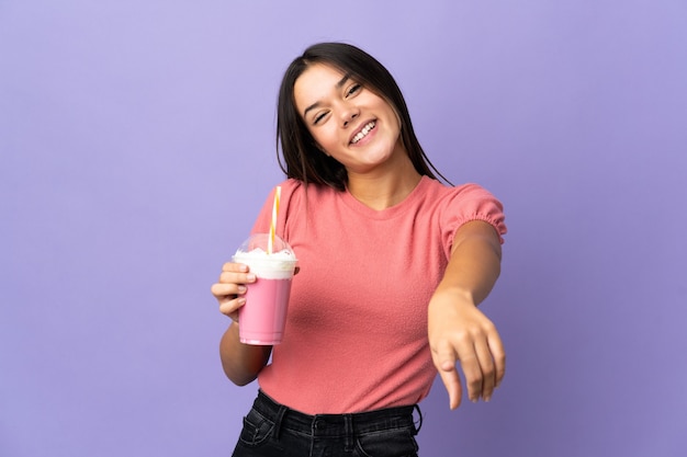 donna che tiene un frappè alla fragola che punta davanti con felice espressione