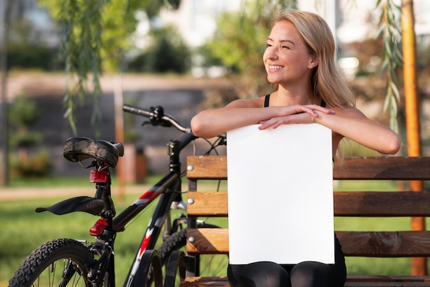 Donna che tiene un libro bianco dello spazio della copia nel parco