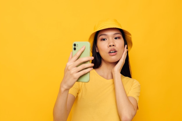 Donna che tiene un telefono che posa lo sfondo giallo della tecnologia di stile di vita inalterato
