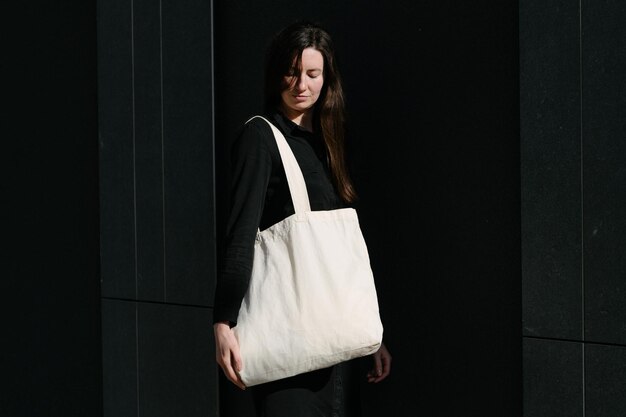 Donna che tiene una borsa ecologica in tessuto bianco sullo sfondo urbano della città Ecologia o concetto di protezione dell'ambiente Borsa ecologica bianca per mock up