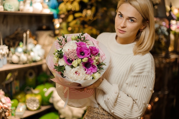 Donna che tiene una composizione natalizia con rose di peonia rosa e bianche viola decorate con foglie verdi