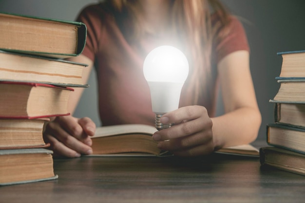 Donna che tiene una lampadina mentre è seduta davanti ai libri. idea concettuale dal libro