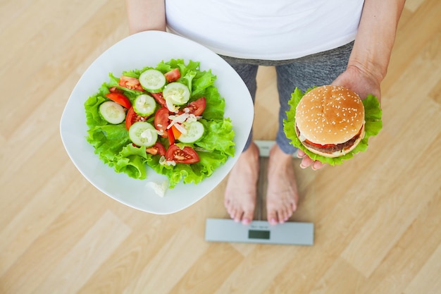 Donna che tiene una scelta di hamburger nocivi e mela fresca