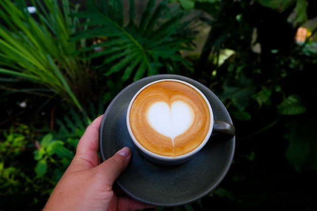 Donna che tiene una tazza grigia di cappuccino con una bella arte del latte a forma di cuore