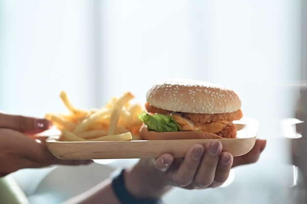 Donna che tiene vassoio di legno con deliziosi hamburger di pesce e patate fritte