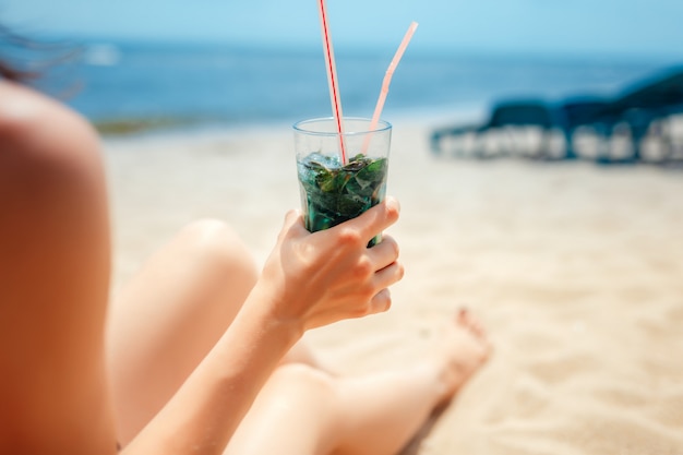 Donna che tiene vetro del cocktail fresco di mojito sulla spiaggia