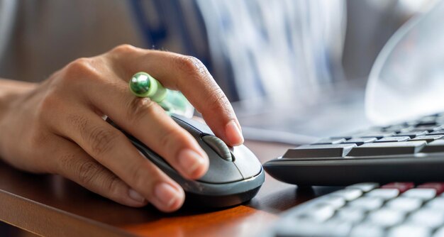 Donna che usa il mouse del PC mentre lavora al computer al tavolo Close up sulla mano di una giovane donna seduta al tavolo di legno nell'ufficio che tiene il mouse del computer portatile che lavora al documento