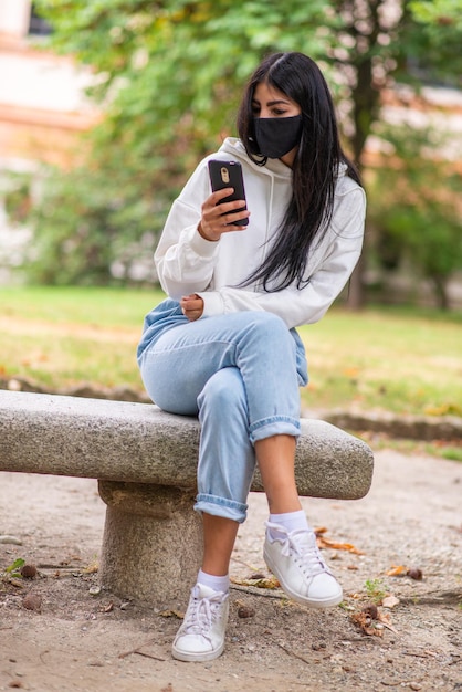 Donna che usa il suo smartphone mentre indossa una maschera da coronavirus
