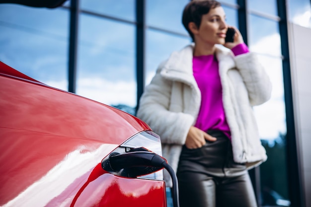 Donna che usa il telefono durante la ricarica dell'auto elettrica vicino all'edificio degli uffici