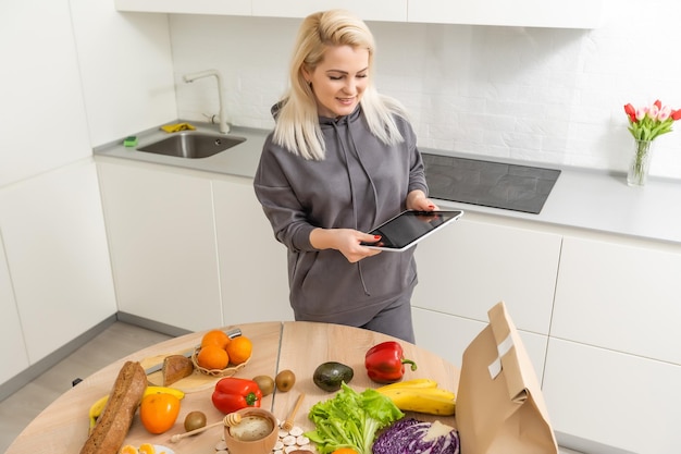 donna che usa tablet nella sua cucina, verdure, cibo sano.