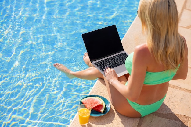 Donna che usa un computer portatile in vacanza vicino alla piscina