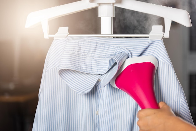 donna che usa un generatore di vapore elettrico a mano mentre è caldo e il vapore esce per la camicia dei vestiti