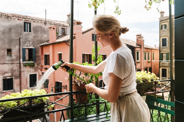 Donna che usa uno spruzzatore per annaffiare per innaffiare le piante su un piccolo balcone