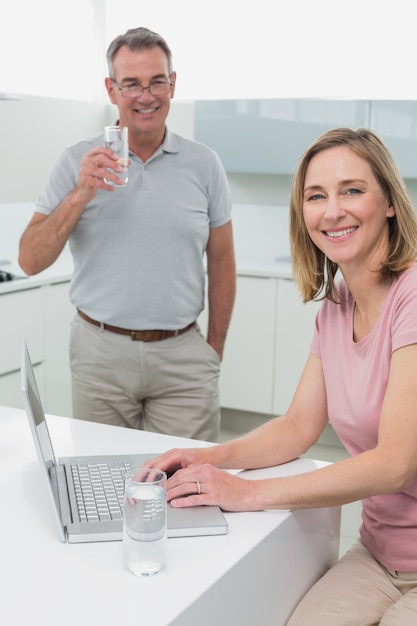 Donna che utilizza computer portatile mentre acqua potabile dell&#39;uomo in cucina