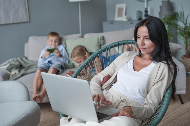 Donna che utilizza il computer portatile con interesse a casa mentre il bambino si rilassa sul divano