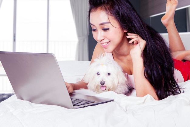 Donna che utilizza il suo laptop con il suo cane in camera da letto