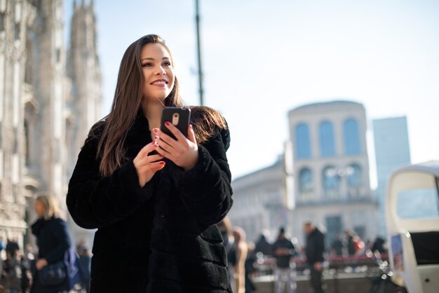 Donna che utilizza il suo smartphone mentre si cammina in una città europea