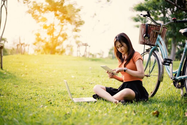 Donna che utilizza la tavoletta e il computer portatile nel parco. Concetto esterno Relax e tecnologia conce