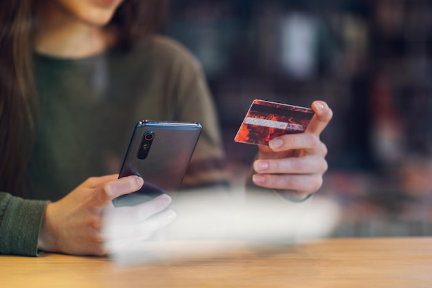 Donna che utilizza smartphone e una carta di credito per lo shopping online in un bar