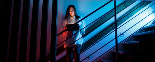Donna che utilizza un tablet mentre si trova in piedi su una scala all'interno di casa di notte
