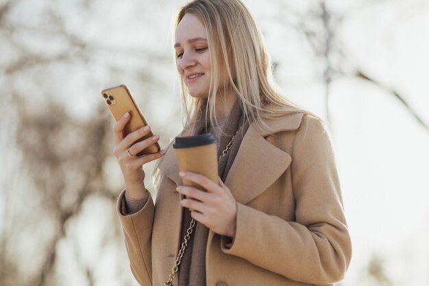 donna che utilizza uno smartphone mentre beve il caffè in città