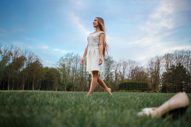 Donna che va a piedi nudi sull'erba verde. Passeggiate serali per la salute