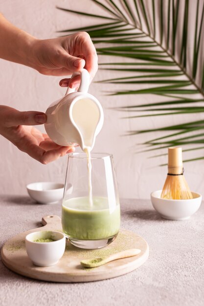 Donna che versa il latte in un bicchiere con tè verde matcha