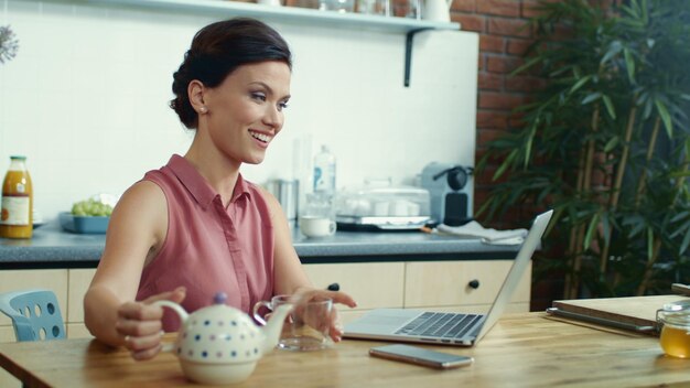 Donna che versa il tè nella tazza durante la videochiamata Ragazza che utilizza il laptop per la chat video