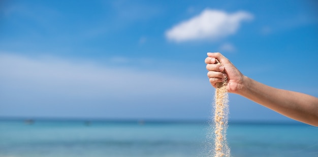 Donna che versa la sabbia dalla mano sulla spiaggia, cielo blu.