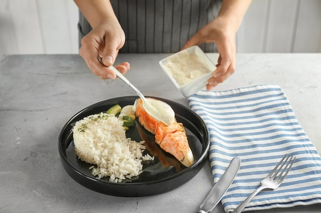 Donna che versa la salsa sul piatto con deliziosi salmone e riso in cucina