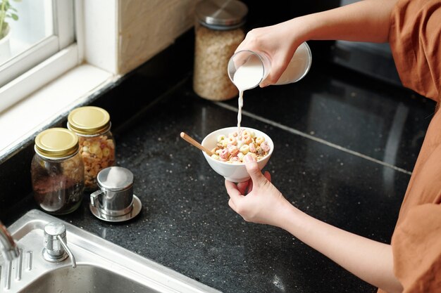 Donna che versa latte fresco in una ciotola di muesli e cornflakes per colazione