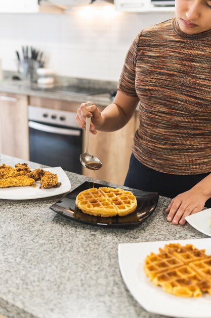 Donna che versa miele e salsa barbecue sui waffle accanto a bistecche fritte di pollo in pastella di cereali