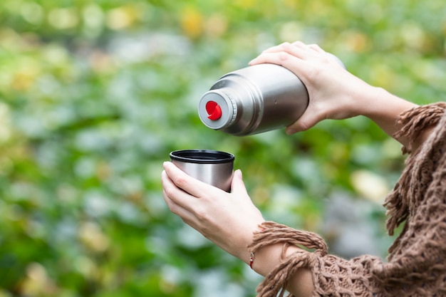 Donna che versa una bevanda calda in tazza dal thermos e che beve tè durante l'escursione.