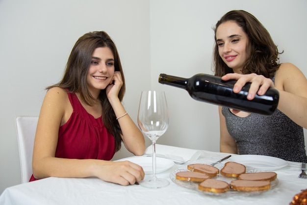 Donna che versa vino in bicchiere da un amico seduto a tavola