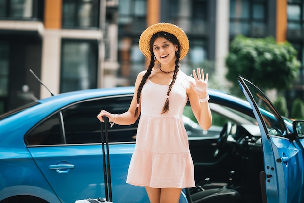 Donna che viaggia con la valigia vicino all'auto a noleggio all'aperto