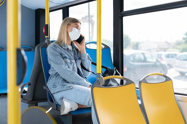 Donna che viaggia in autobus pubblico parla al telefono mentre indossa una maschera medica per protezione