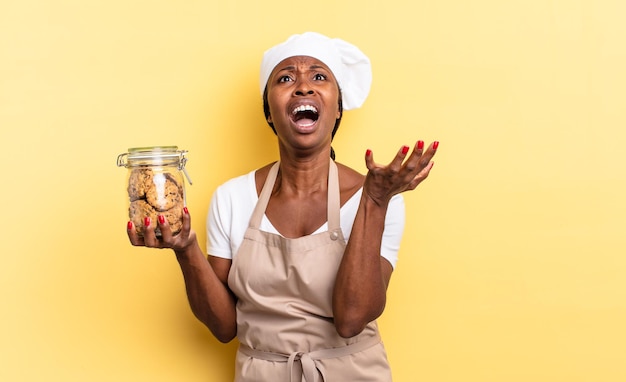 Donna chef afro nera che sembra disperata e frustrata, stressata, infelice e infastidita, urlando e urlando. concetto di biscotti