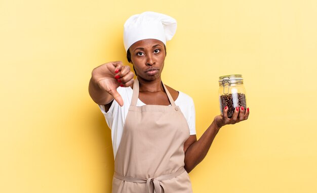 Donna chef afro nera che si sente arrabbiata, arrabbiata, infastidita, delusa o scontenta, mostrando il pollice verso il basso con uno sguardo serio. concetto di chicchi di caffè