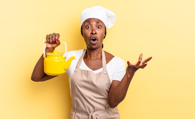 Donna chef afro nera che si sente estremamente scioccata e sorpresa, ansiosa e in preda al panico, con uno sguardo stressato e inorridito. concetto di teiera