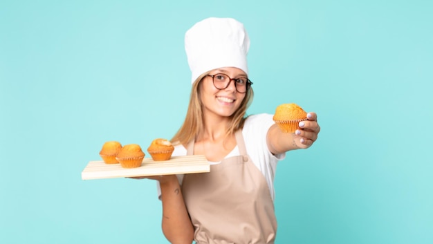 Donna chef bionda abbastanza giovane che tiene in mano un vassoio di muffin