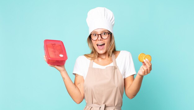 Donna chef bionda abbastanza giovane e con in mano un tupperware