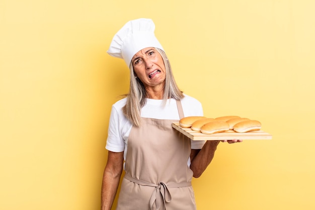 Donna chef di mezza età che si sente perplessa e confusa con un'espressione sbalordita che guarda qualcosa di inaspettato e tiene in mano un vassoio per il pane