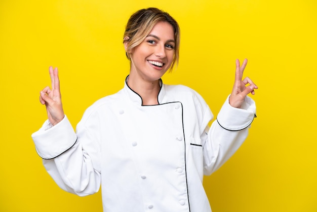 Donna chef uruguaiana isolata su sfondo giallo che mostra il segno della vittoria con entrambe le mani