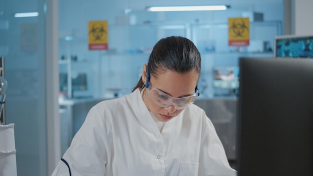 Donna chimica che prende appunti e utilizza il computer per l'esperimento in laboratorio. Specialista che lavora sullo sviluppo scientifico, svolgendo studi di ricerca e scrivendo su carta nel laboratorio di scienze.