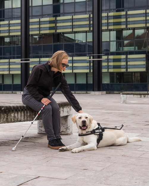 Donna cieca o non vedente che si riposa con un cane guida sulla panchina