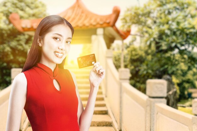 Donna cinese asiatica in un vestito cheongsam che tiene la carta di credito. Buon Capodanno cinese