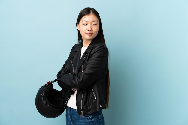 Donna cinese che tiene un casco del motociclo sopra la risata blu